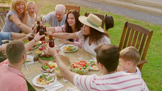 Family and Friends Gathered Together at the Table Raise Glasses and Bottles To Make a Toast and Clink Glasses