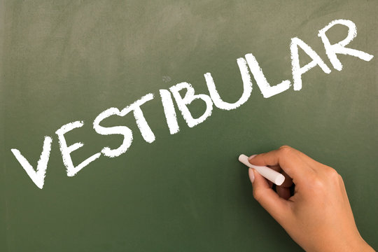 Female hand writing with chalk on empty green chalkboard. (translation portuguese:  entrance exam)