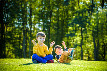 Two Caucasian boy brother friends sitting down on fresh green grass field and make meditation dressed in casual clothes.