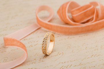 Pink gold wedding ring with diamonds on beige background with ribbon