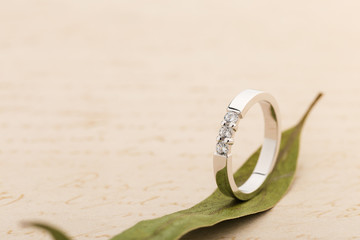 White gold wedding ring with diamonds on leaf on beige background