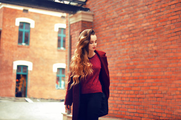 Outdoors lifestyle fashion portrait of brunette girl. Wearing stylish red coat. Walking to the city street. Long curly light hair. Joyful and cheerful woman. Street fashion concept. High fashion photo