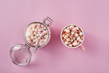 View from above at marshmallows in mug and glass jar on pink background