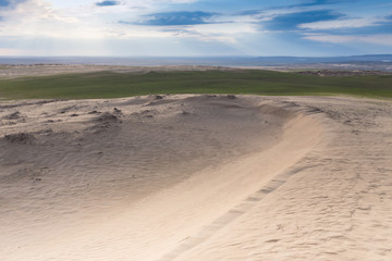 Green grass and cracked desert land over dramatic clouds