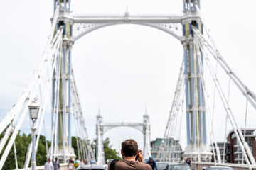 London, UK back of man tourist taking pictures view of city Albert bridge with camera on street...