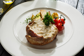 Pork with white mushroom sauce garnished with fried potatoes and cherry tomatoes.
