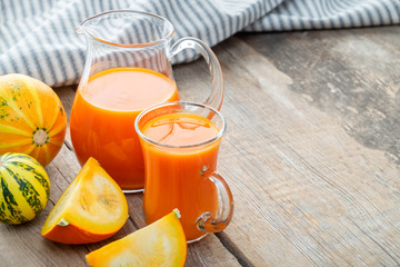 Mug and jug of fresh pumpkin juice and pumpkins on table. Copy space for text.