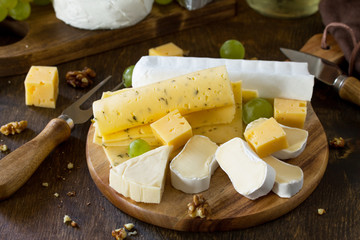 Cheese plate. Assortment of cheeses, grapes and nuts on dark rustic wooden table.