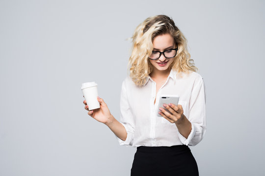 Portrait Of A Satisfied Young Business Woman Using Mobile Phone While Holding Cup Of Coffee To Go Over White Background