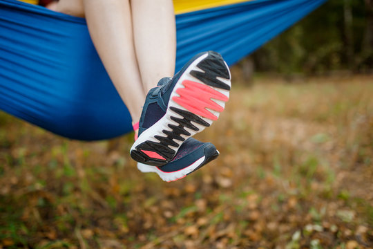 Image of woman with hanging legs in sneakers lying in hammock in woods