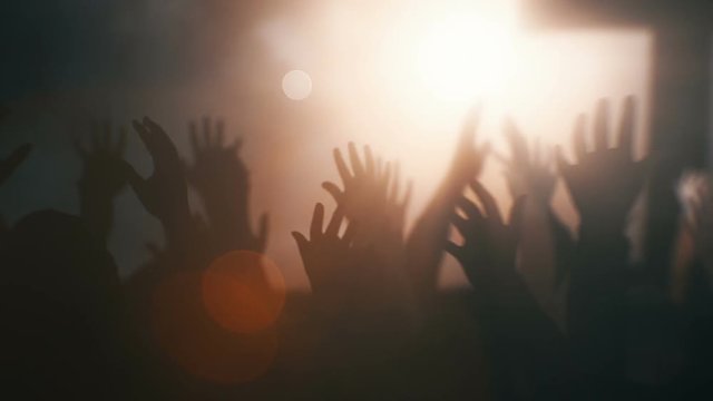 Silhouettes of hands raised in worship with light rays and Cross.