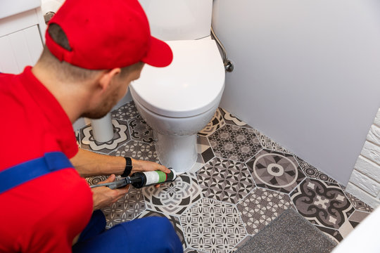 plumber applying silicone sealant around water closet