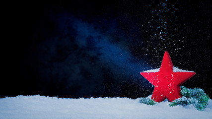 Roter Stern mit Tannenzweig vor tiefblauem Hintergrund mit Schnee