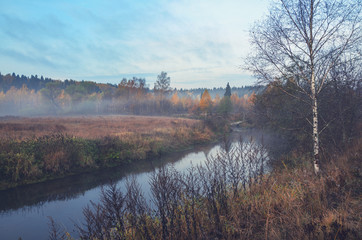 Foggy autumn landscape with small forest river.