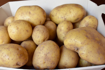 WHITE BOX PLENTY OF RAW POTATOES WITH THE BIGGEST POTATO AT THE RIGHT DOWN CORNER 