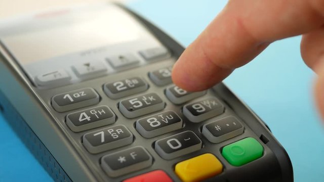 Credit card reader machine at bar counter with male holding credit card. Hand of customer paying with contactless credit card with NFC technology on blue background. Finger entering the PIN code