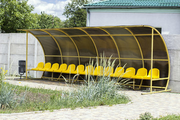 seat bench and coach on a yellow-colored football field against a concrete wall