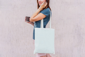 Young woman with white cotton bag and paper coffee cup in her hands.