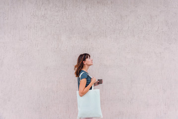 Young woman with white cotton bag and paper coffee cup in her hands.