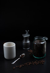 a cup of coffee and a jar of coffee beans on dark table