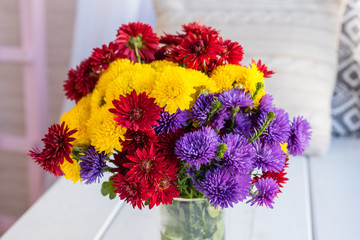 Beautiful bright colorful bouquet of multi-colored flowers in a glass vase on a wooden table about a window