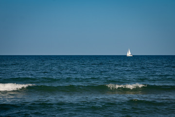 Yacht with white sails away into the sea. Waves in the foreground.
