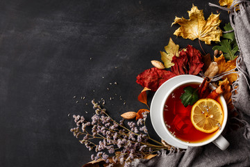Autumn composition. A cup of fragrant tea with lemon on a dark table with autumn leaves and flowers.