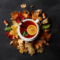 Autumn composition. A cup of fragrant tea with lemon on a dark table with autumn leaves and flowers.