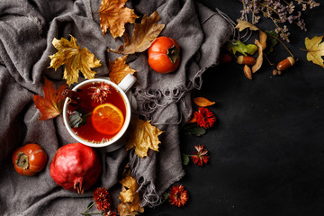 Autumn composition. A cup of fragrant tea with lemon on a dark table with autumn leaves and flowers.