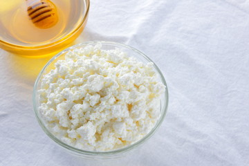 Cottage cheese on white background. Fresh cottage cheese and honey on white cloth. Soft cheese in glassware. Dairy product for breakfast. Copy space