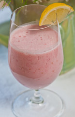 Top view, close distance of a clear glass of raspberry coconut smoothie, with a slice of lemon on a white table cloth