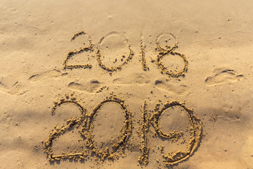 Concept of Happy New Year 2019 is coming and leaving year of 2018. Text on the sea beach and footprints on the sand. Wave water covering digits inscription. Meet at a tropical resort in Thailand.