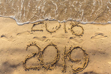 Concept of Happy New Year 2019 is coming and leaving year of 2018. Text on the sea beach and footprints on the sand. Wave water covering digits inscription. Meet at a tropical resort in Thailand.