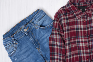 Blue jeans and red checkered shirt on wooden background. Fashionable concept