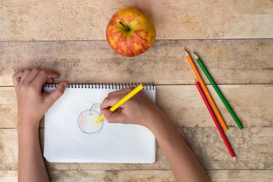 Children's hands draw an apple with colored pencils. Top view