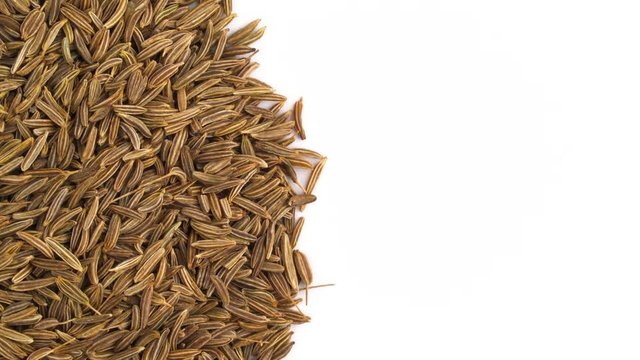 Half frame. View from above of a circle shaped caraway seeds heap. Rotating on the turntable. Isolated on the white background. Close up. Macro. Copy Space.