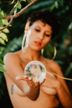 Topless woman holding glass sphere in woods