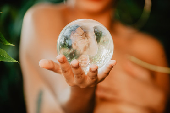 Topless woman holding glass sphere in woods