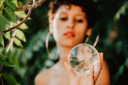 Topless woman holding glass sphere in woods