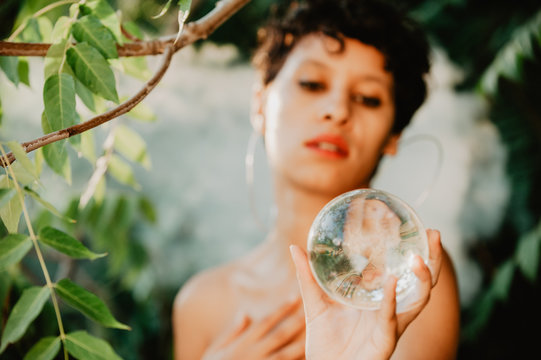 Topless woman holding glass sphere in woods