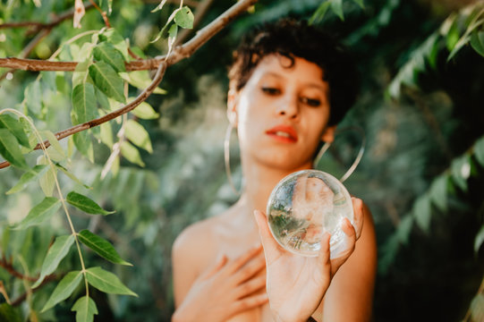 Topless woman holding glass sphere in woods