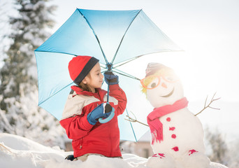 Child with snowman on snow with umbrella