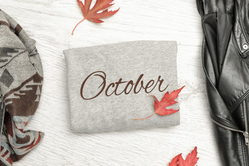 Gray sweater with inscription October, a black jacket, scarf and autumn leaves. Fashionable concept