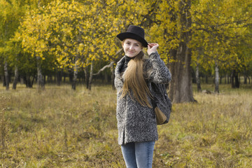 Smiling girl in a hat standing in the autumn forest. Back view