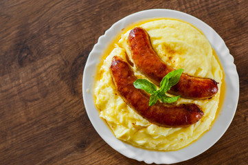 fried meat sausages with mashed potatoes in white plate on wooden table background