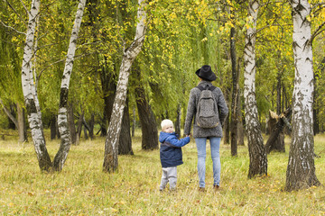 Fototapeta premium Mom and son are walking in the autumn forest. View from the back