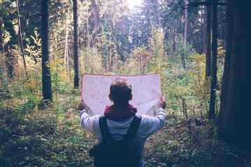 Young traveler man with map, backpack at autumn green forest in sunny day. Relaxing outdoor, hiking lifestyle
