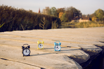 Three small alarm retro clocks on wooden surface. Autumn abstract photo.