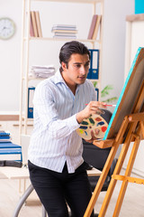 Young handsome employee enjoying painting at the office 