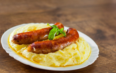 fried meat sausages with mashed potatoes in white plate on wooden table background